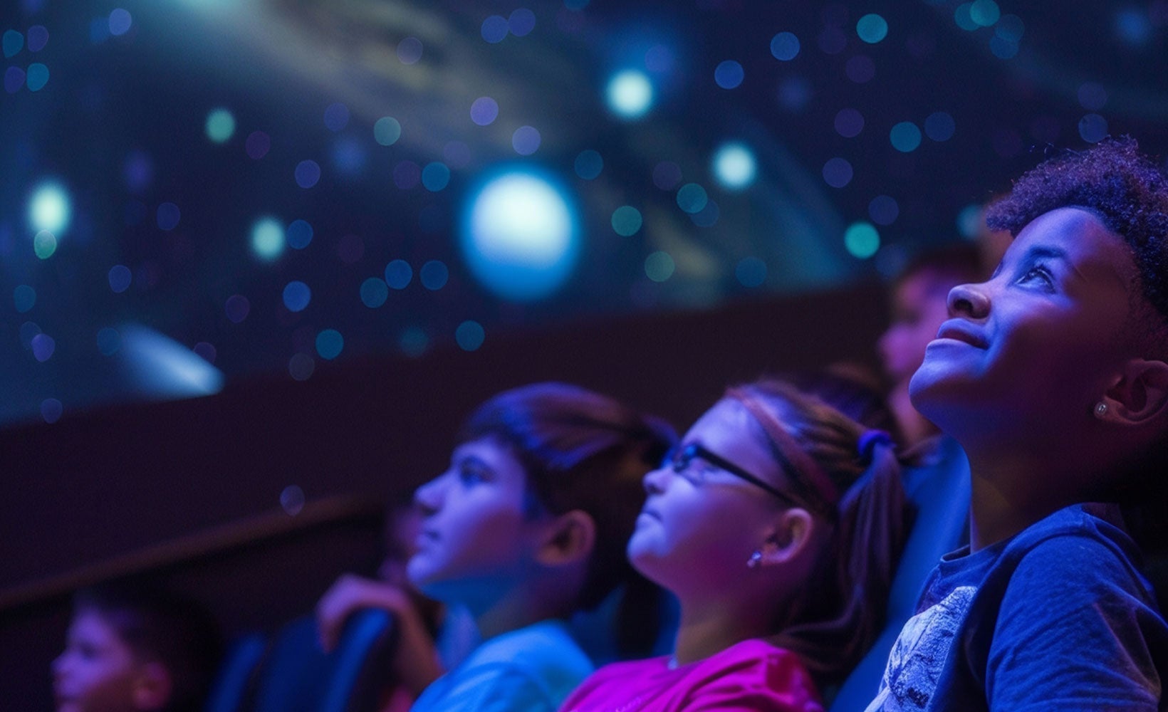 Kids look up at space at a planetarium auditorium.