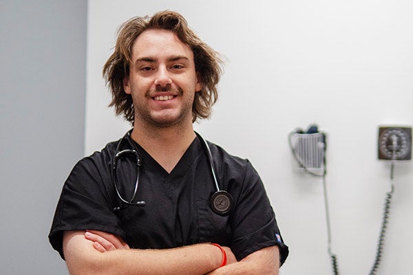Young man smiles while wearing scrubs and a stethoscope.