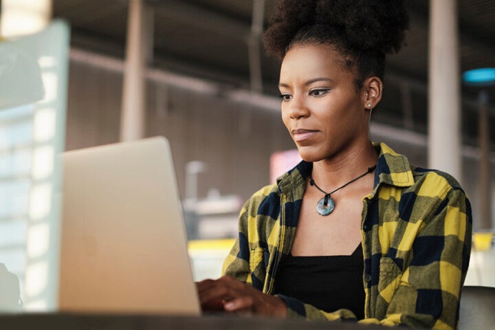 A woman looks down at a laptop as she sits in a modern and exposed brick urban style building