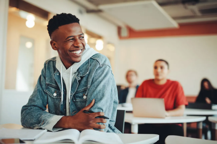 Male student smiling at desk in class with open books