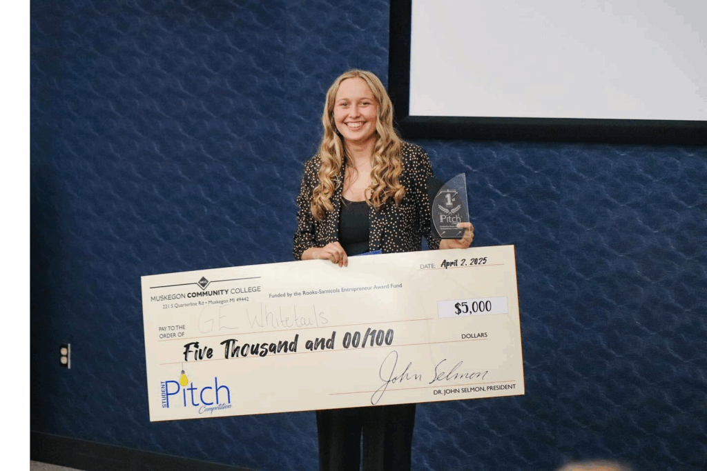 A student holds a large ceremonial check for $5000 and smiles for the camera while holding a trophy.