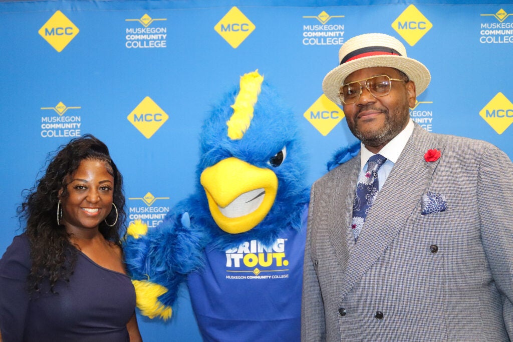 A man wearing a hat and a woman pose with MCC Mascot Jay.