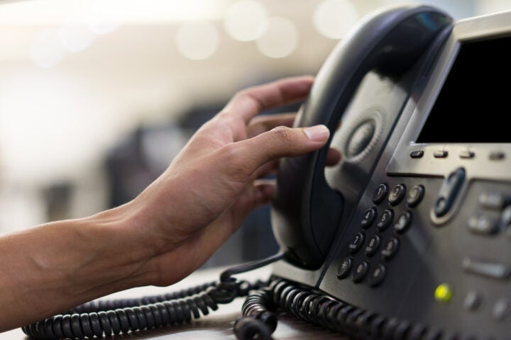 Picture of a hand picking up an office phone.