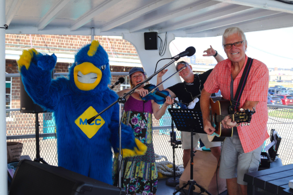 Group of musicians celebrate MCC's centennial. They are on a boat with Jay the Jayhawk
