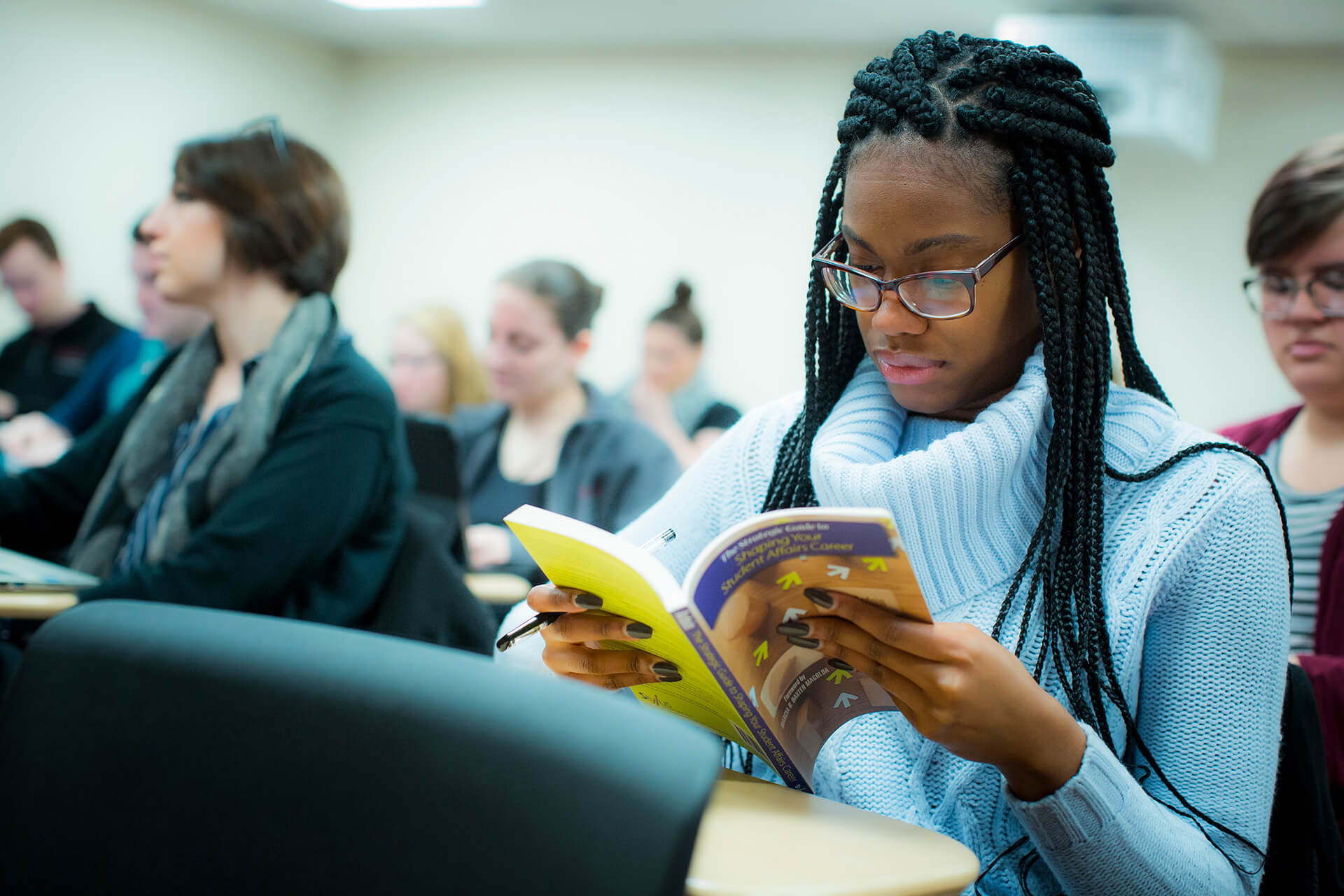 A girl reads a catalog book in class and ponders what classes to take