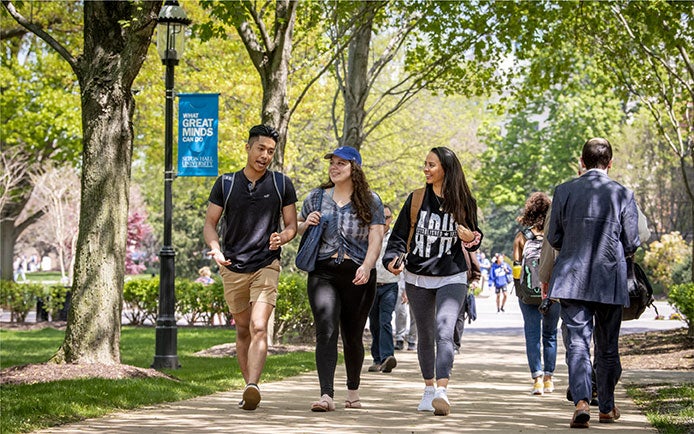 Students walking outside the main building during spring, trees are in the background.