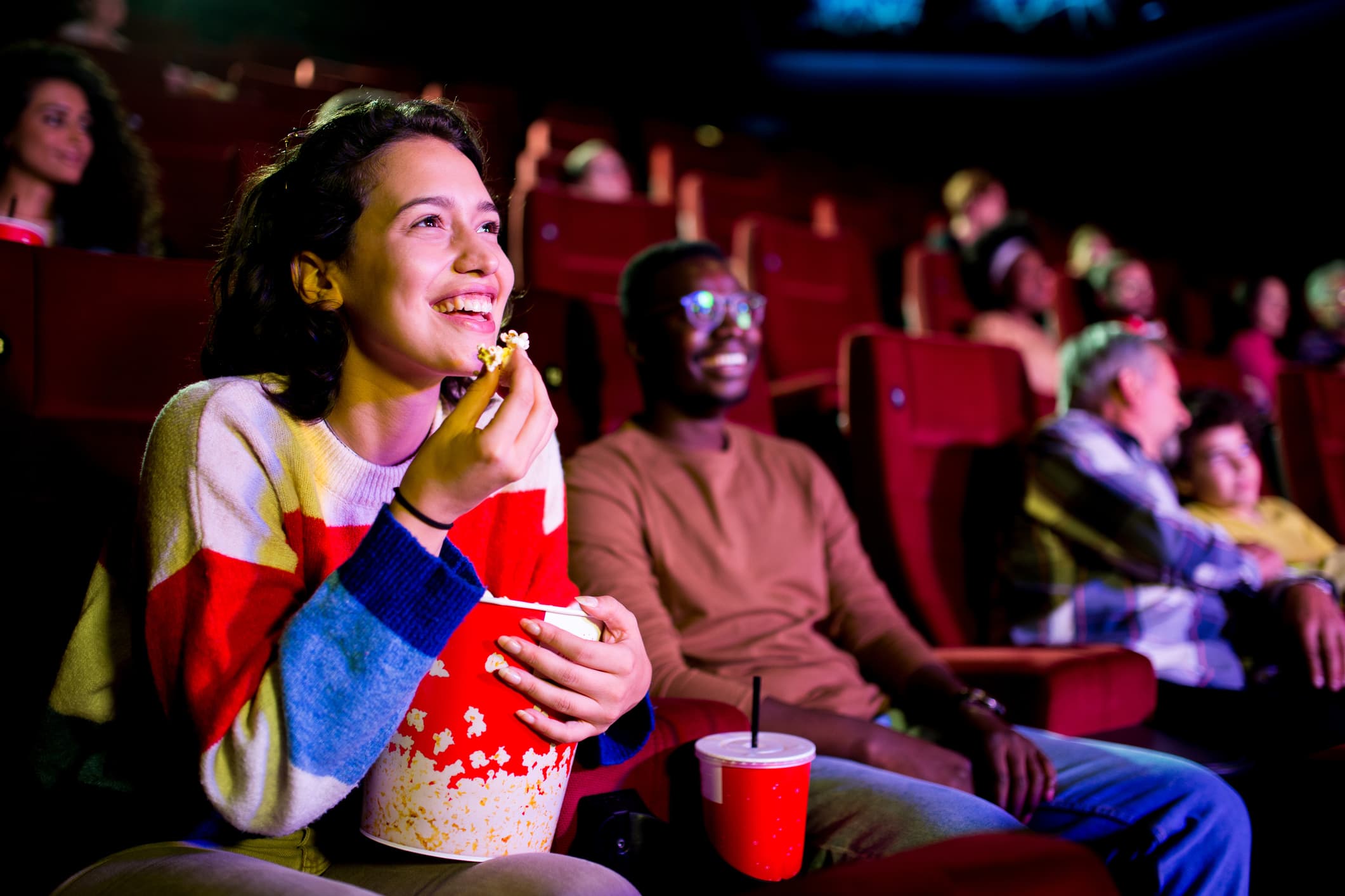 A girl eats popcorn and smiles as she watches a movie.