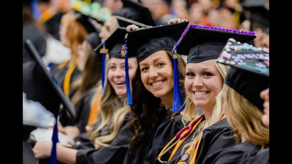 Girls smile for the camera in graduation robes at Commencement ceremony.