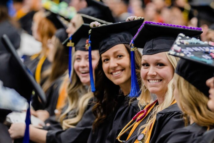 Girls smile for the camera in graduation robes at Commencement ceremony.