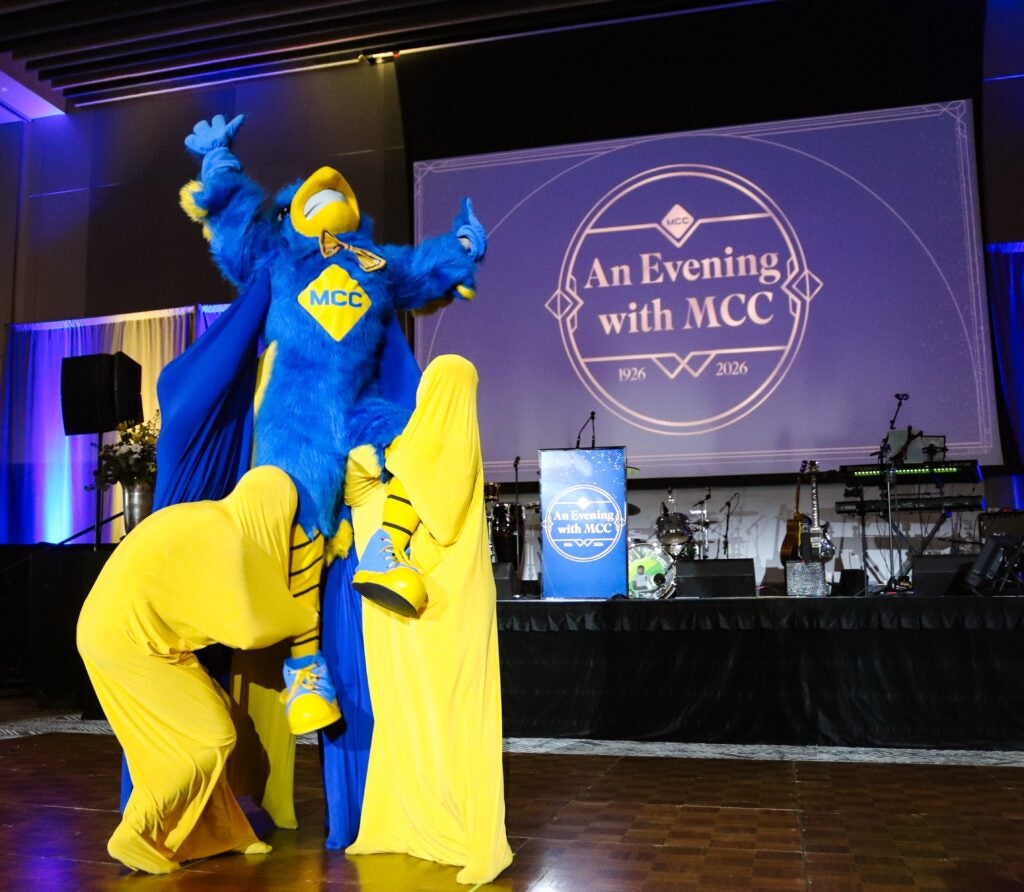 Jay the Jayhawk mascot is hoisted in the air by two dancers wearing all yellow.